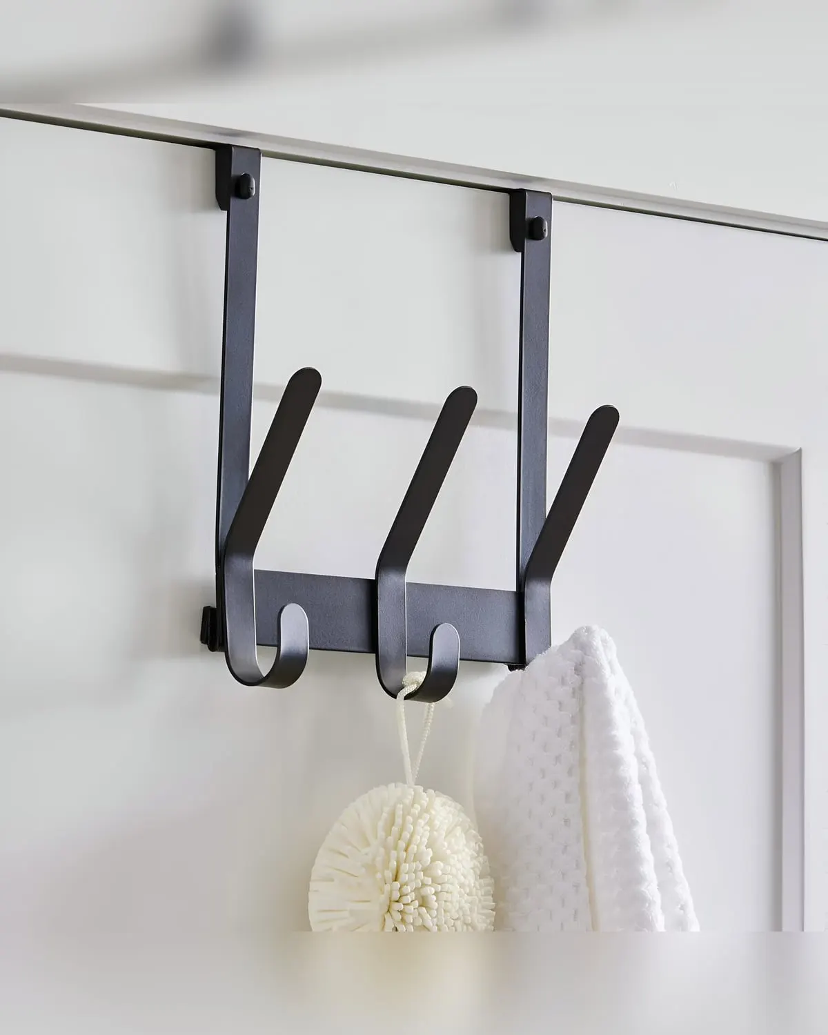 Matte black over-the-door hook rack with towels hanging on a bathroom door