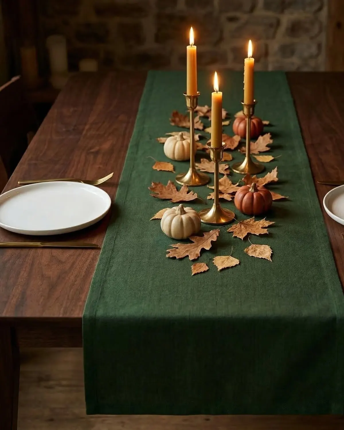 Green linen table runner down a wooden dining table set with pumpkins, dried leaves and lit taper candles
