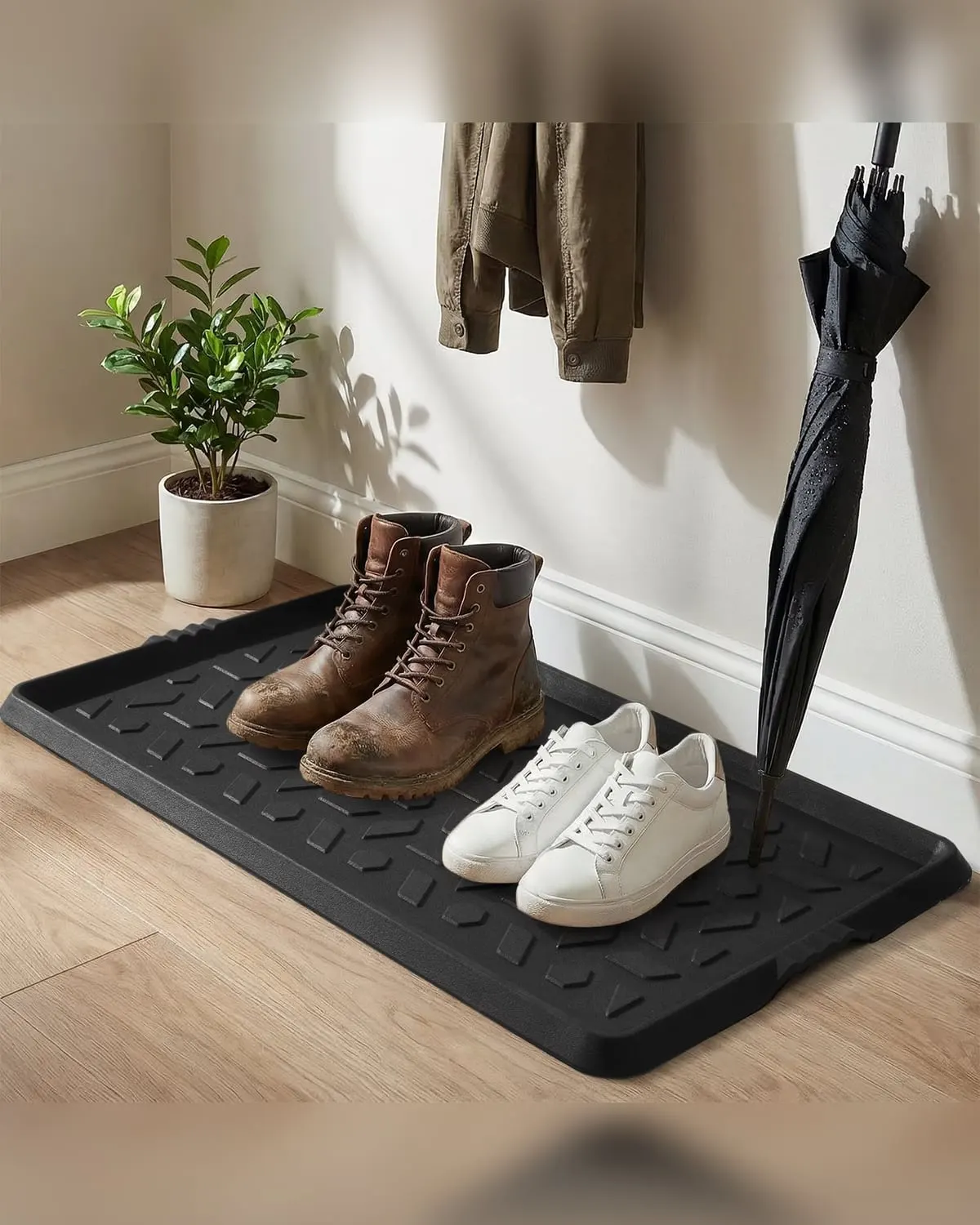 Black rubber boot tray with a raised lip holding muddy boots, trainers and a wet umbrella by an entry door