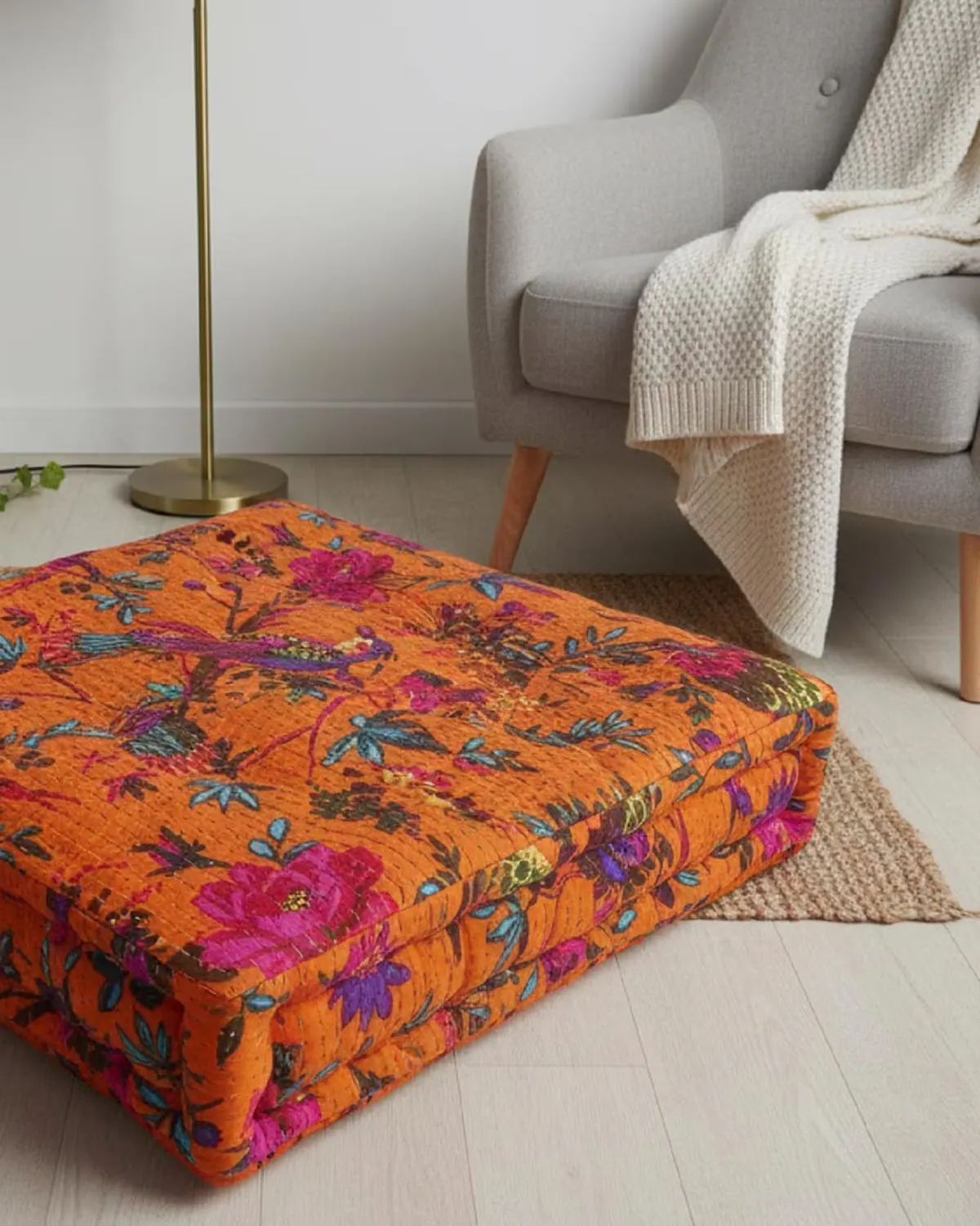 Handmade kantha patchwork floor cushion in a bright orange print beside an armchair