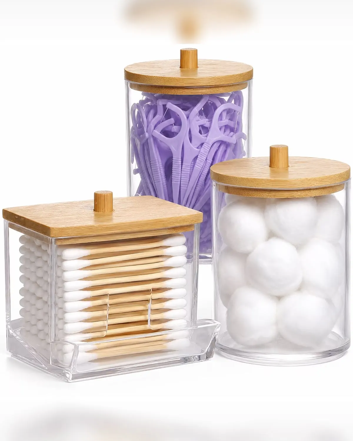 Glass apothecary jars with bamboo lids holding cotton balls on a bathroom shelf