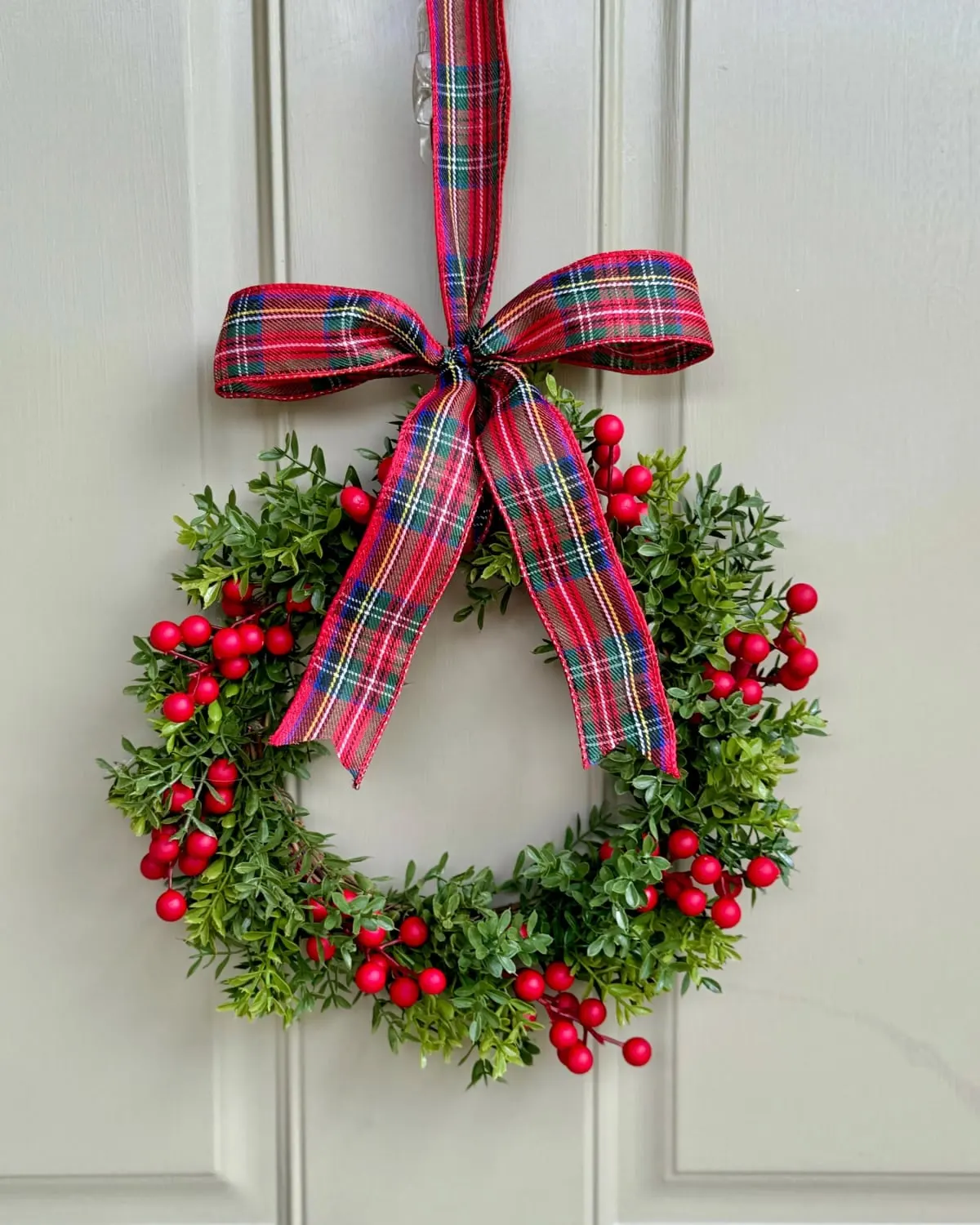 Small handmade boxwood and berry Christmas wreath on a cabinet