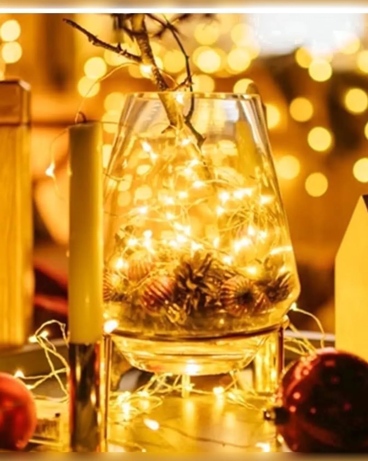 Warm white battery fairy lights coiled inside a glass vase beside a lit candle