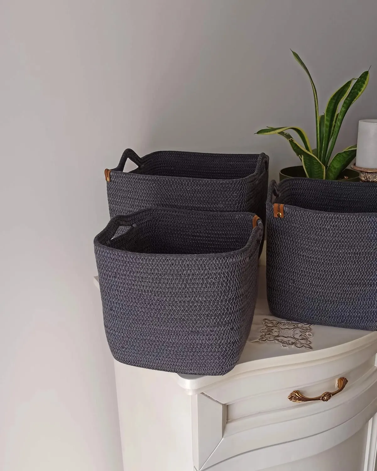 Three handwoven grey cotton rope storage baskets with handles on top of a cabinet