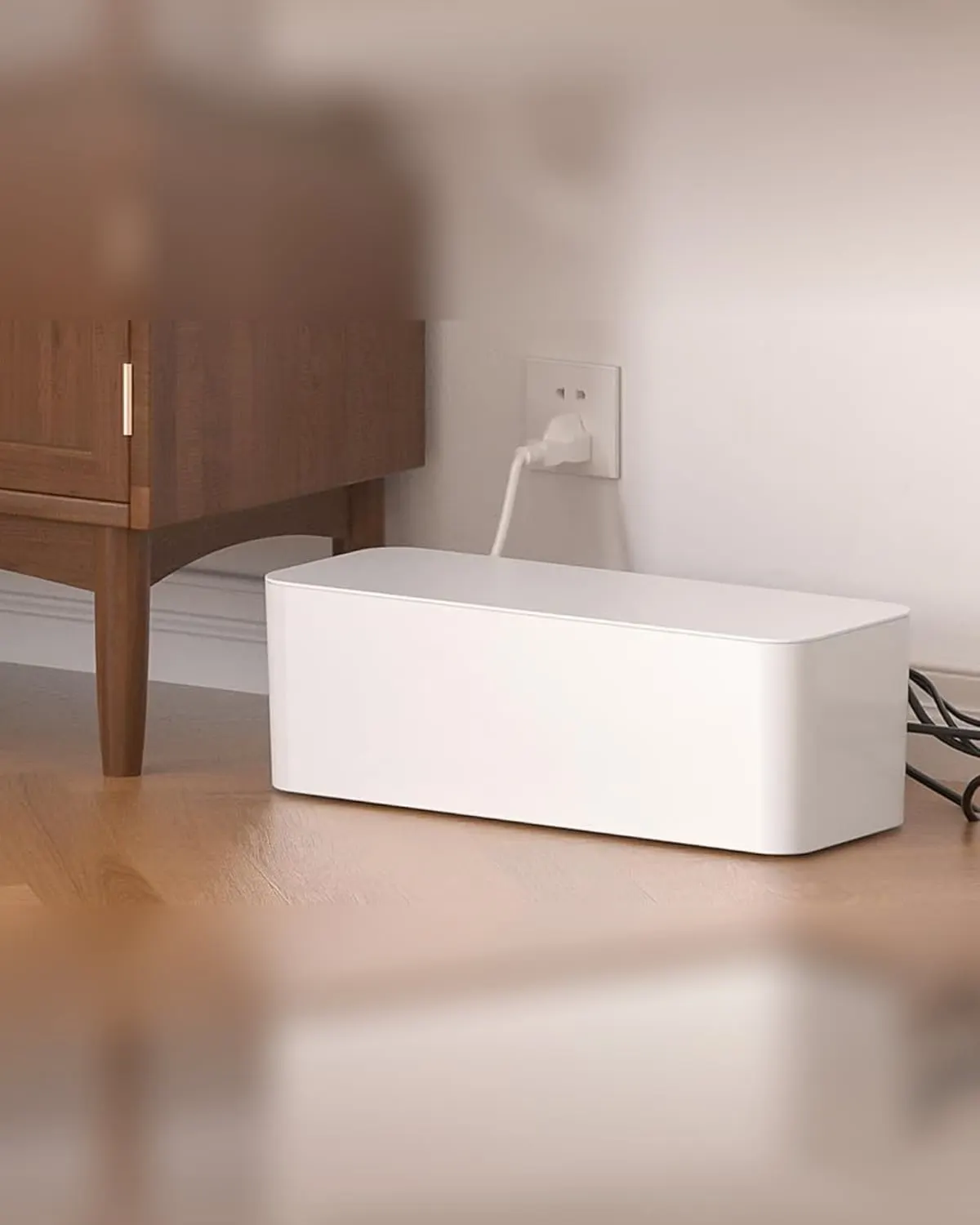 White cable management box hiding a power strip and cords beside a wooden console